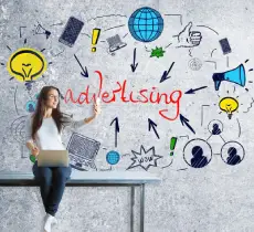 A woman sits on a table holding a laptop and reaching out, with the word "advertising" and various marketing icons drawn on a wall behind her.